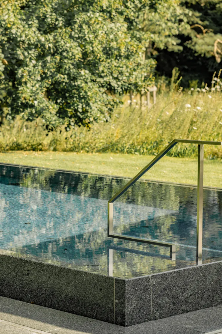 Ein Natursteinpool aus massiven Granit mit elegenaten Geländer und schöner Gartenanlage